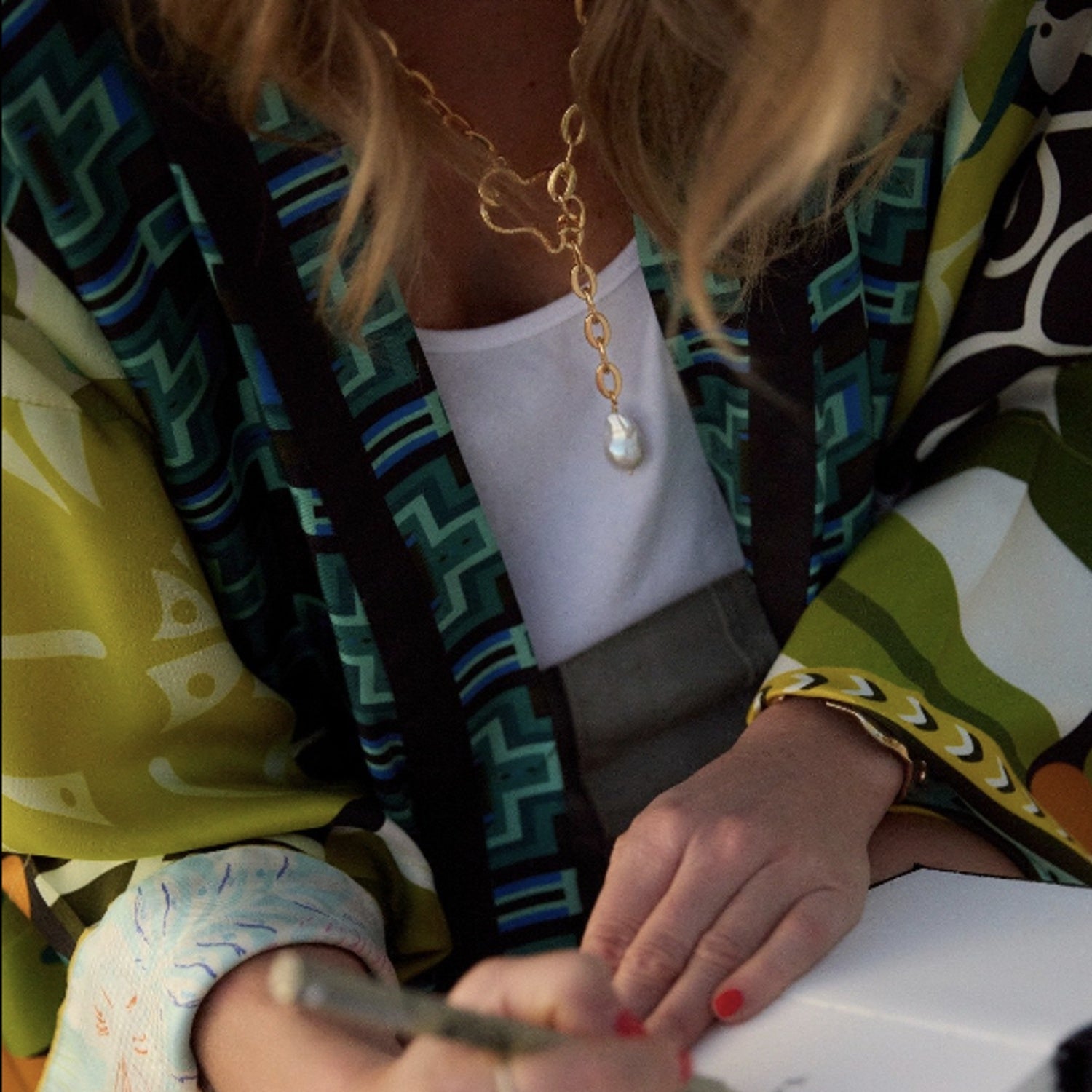 Person wearing a colorful patterned garment with a gold necklace and white sleeve.