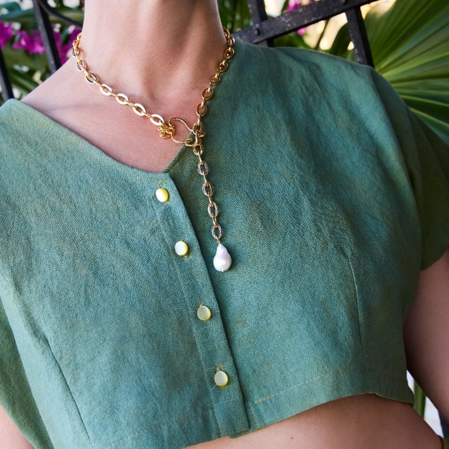Gold chain necklace with a pendant on a person wearing a green shirt.