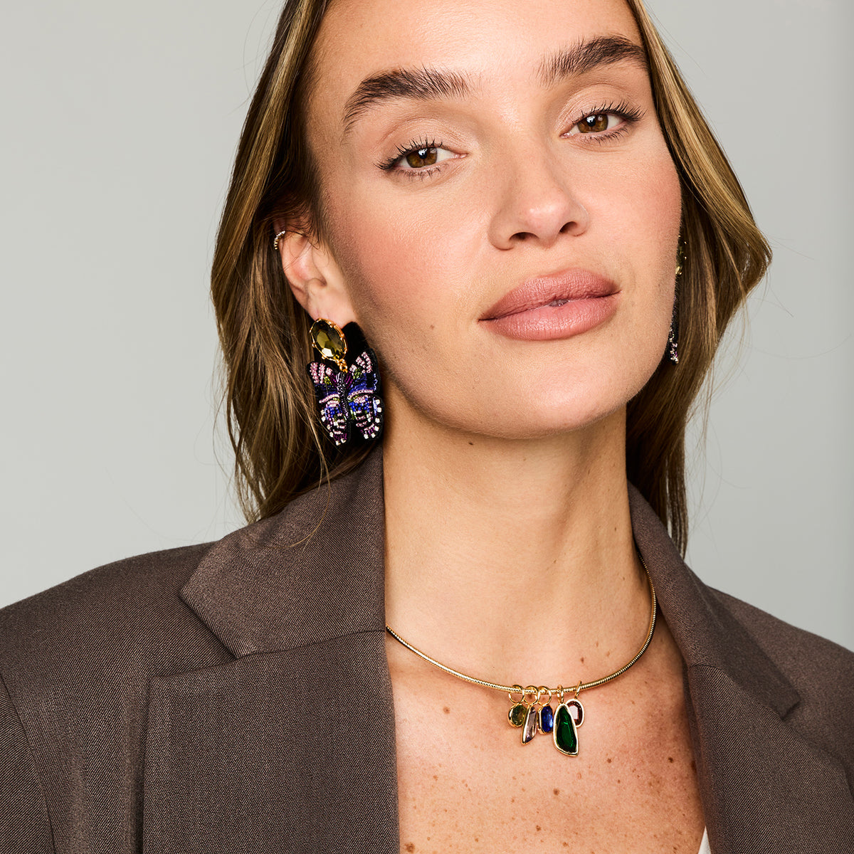 Multicolor butterfly-shaped statement earrings featuring purple, blue, and green beadwork with gold-tone details on Model straight on 