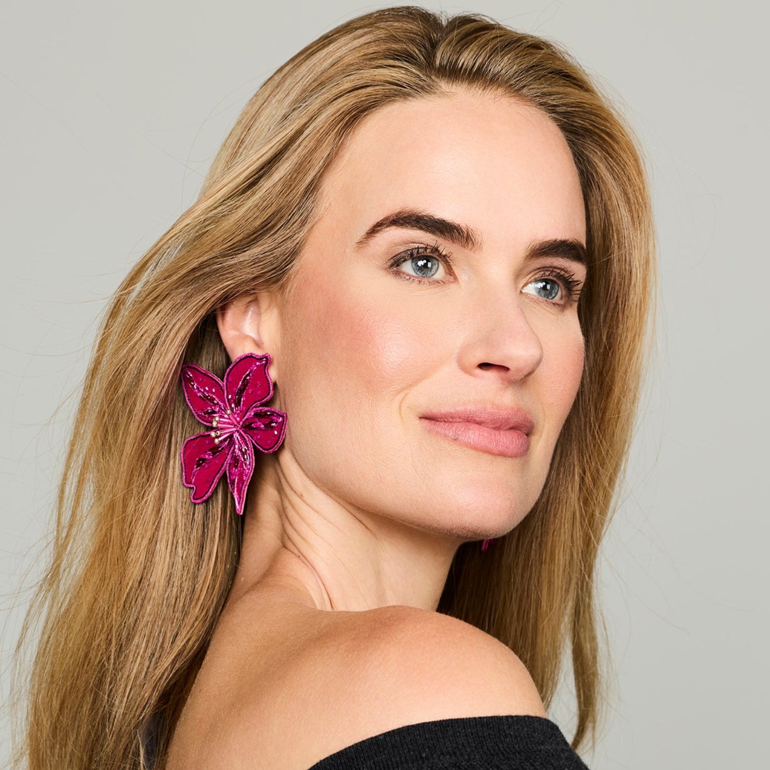 Magenta flower-shaped statement earrings featuring layered petals and intricate beadwork on model