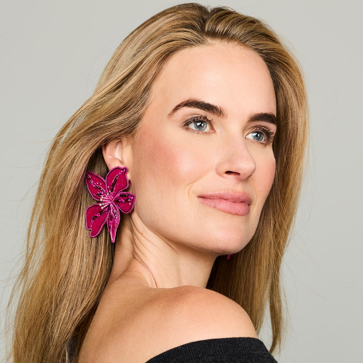 Magenta flower-shaped statement earrings featuring layered petals and intricate beadwork on model