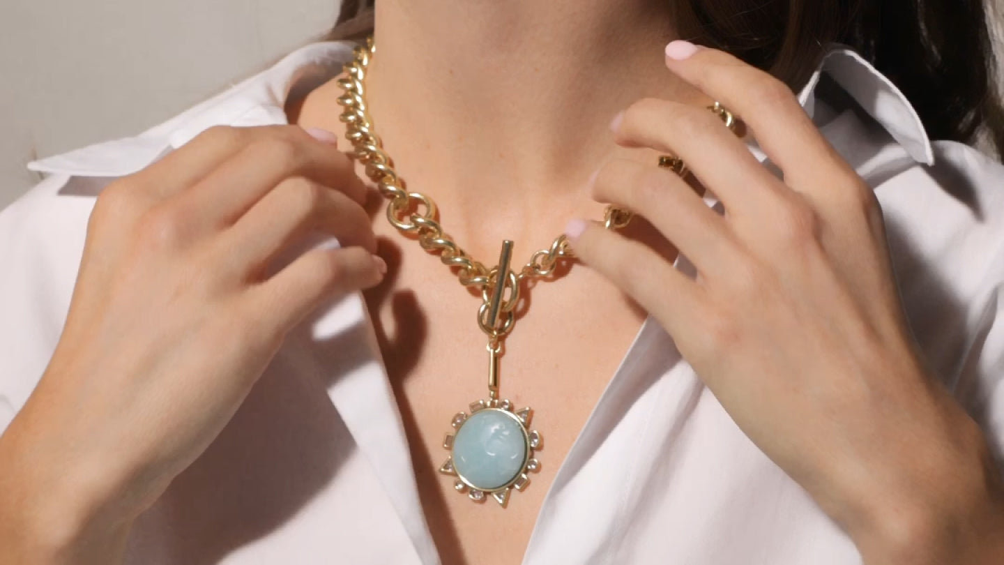 Person wearing a gold necklace with a blue pendant