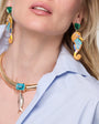 Close-up of a person wearing gold and turquoise Genesis Earrings with a plain background