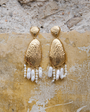 Gold earrings with pearl-like beads on a textured stone surface