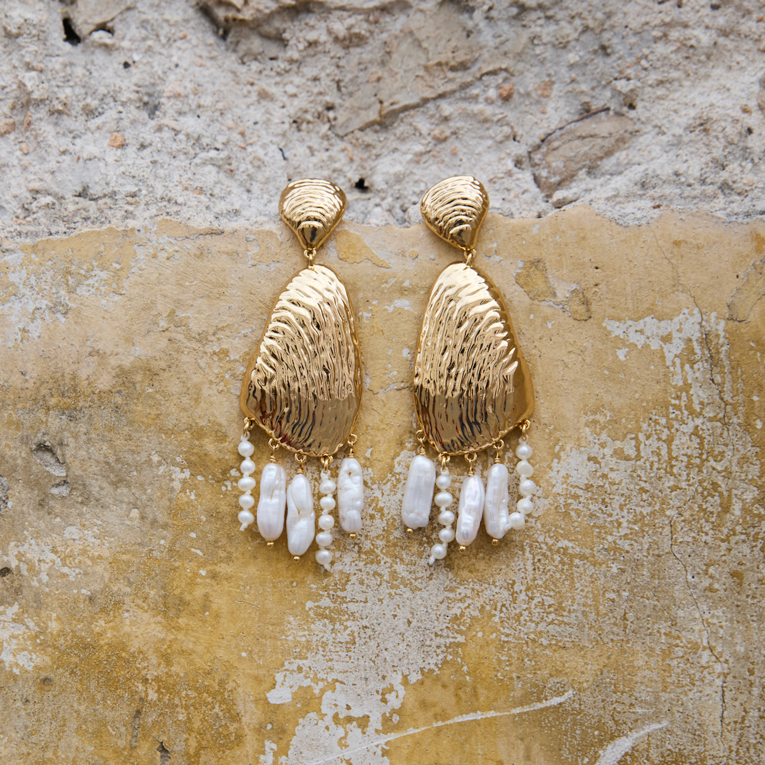 Gold earrings with pearl-like beads on a textured stone surface