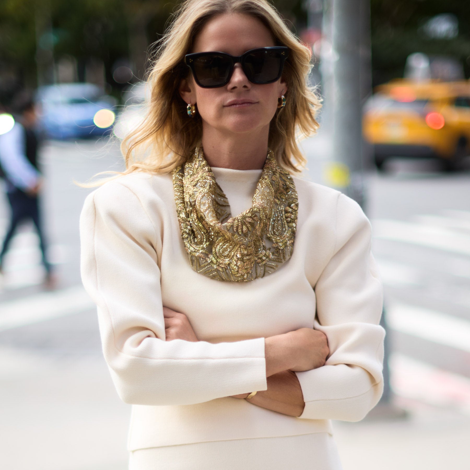 Maggie wearing a white outfit with a gold scarf in an urban setting