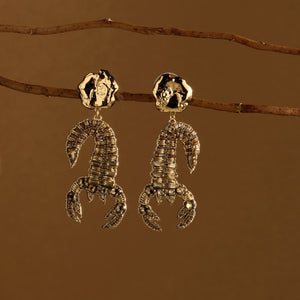 Gold Beaded Scorpion Drop Earrings Staged on Branch with Brown Background