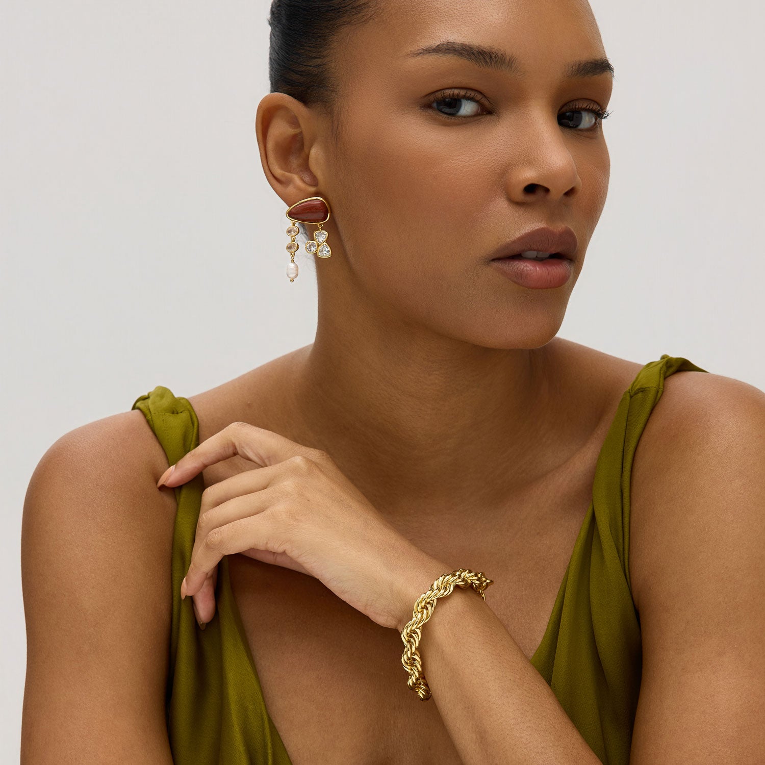 gold chain bracelet styled on model wearing red stone and crystal drop earrings