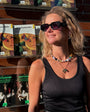 Woman standing in front of a display of 'Apauro Lamento' books or packaging wearing beaded strand necklace and charm necklace