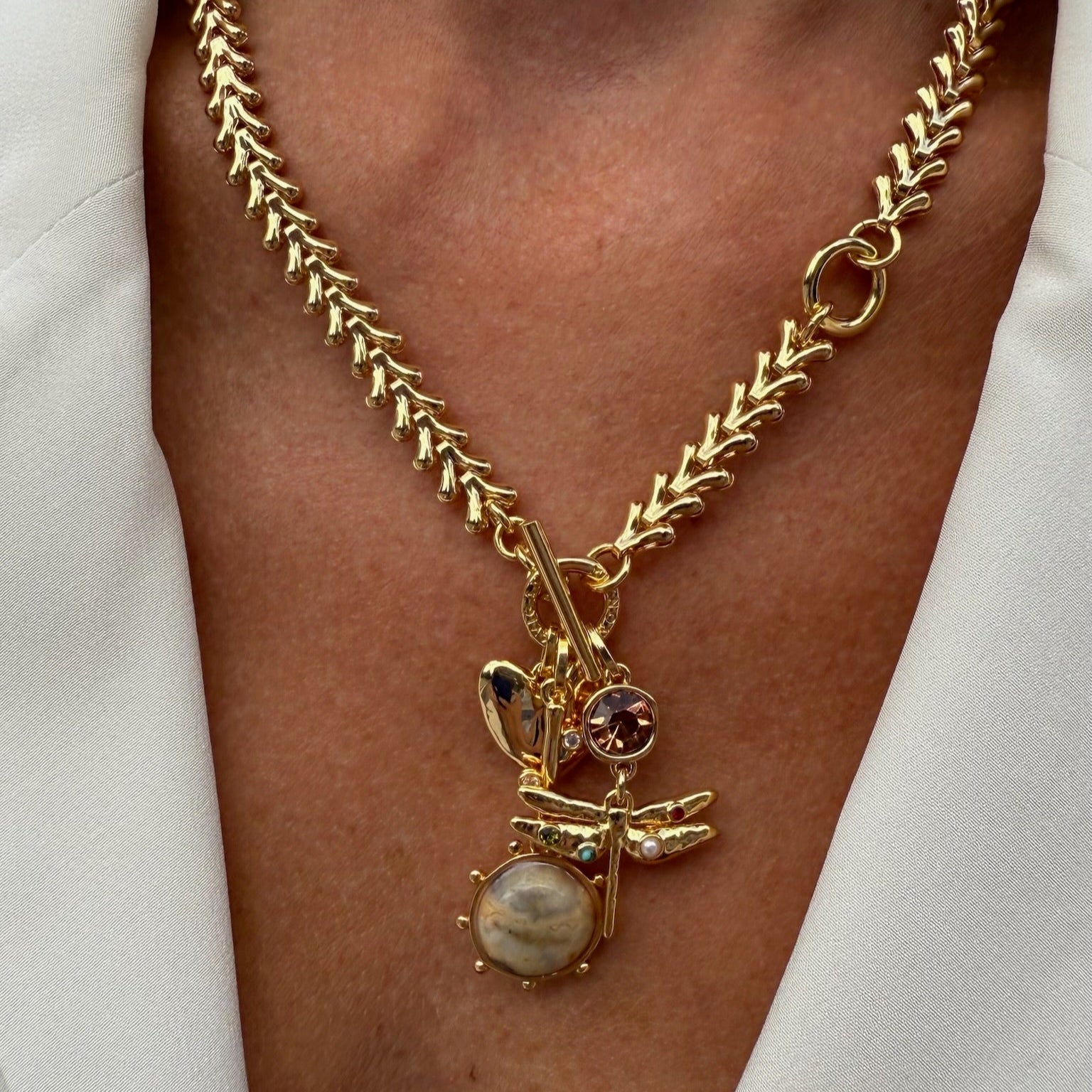 Gold necklace with a pendant on a person wearing a white shirt.