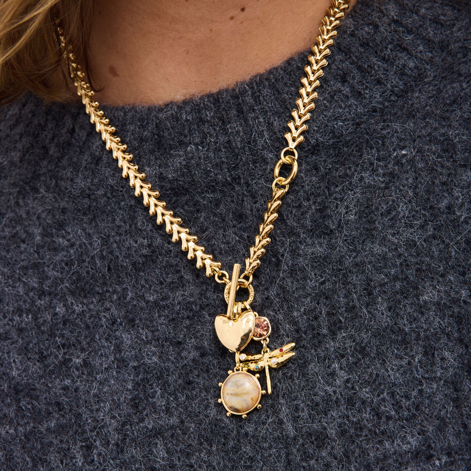Gold necklace with a pendant on a person wearing a grey sweater