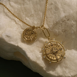 Gold Coin and Compass Pendant Necklace Staged on Stone