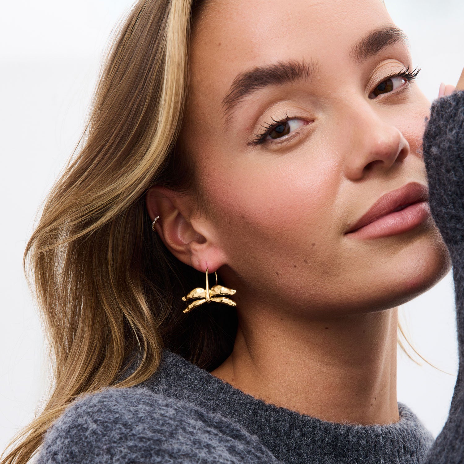 Gold dragonfly drop earrings styled on model in grey sweater