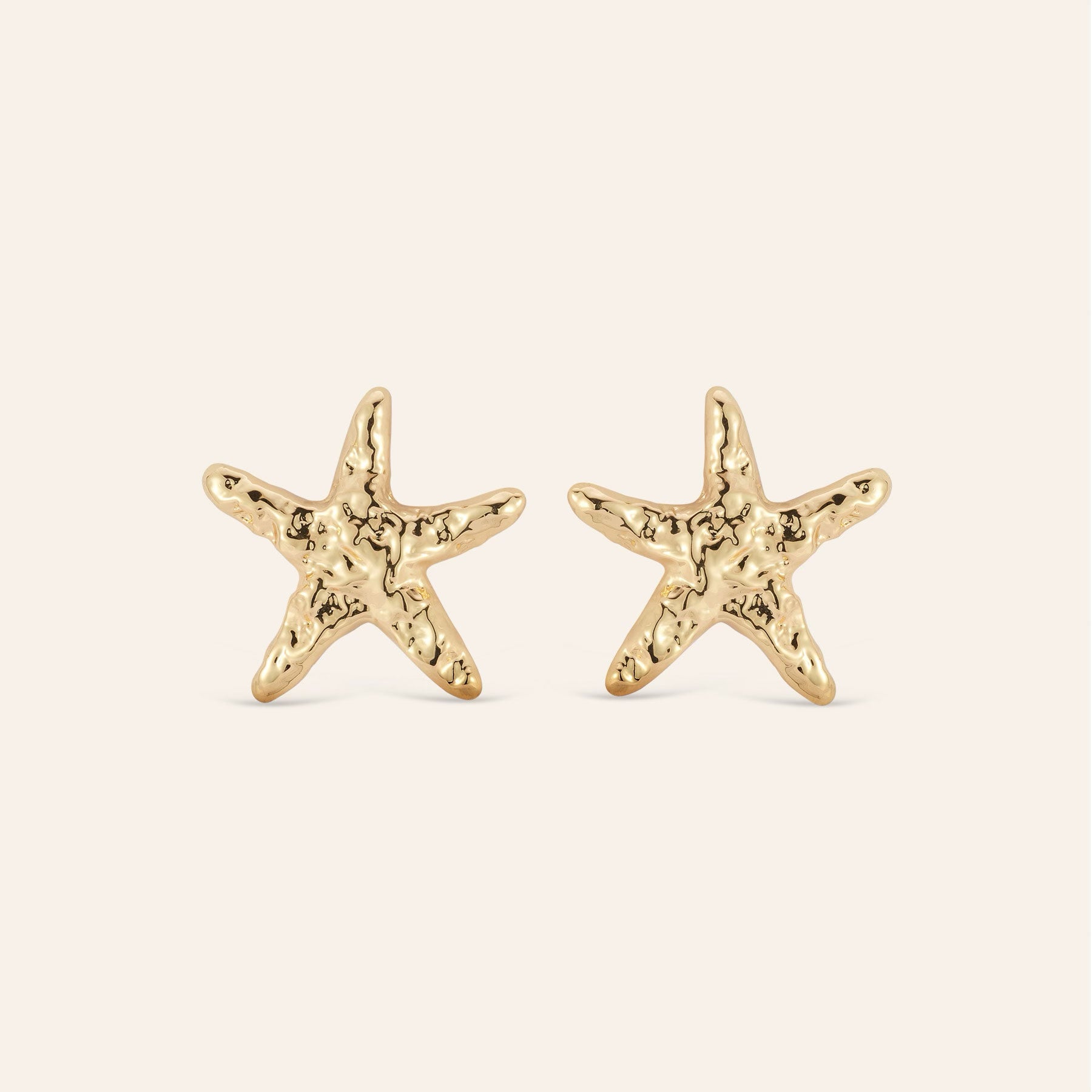 Hammered Gold Star Fish Stud Earrings on Cream Background