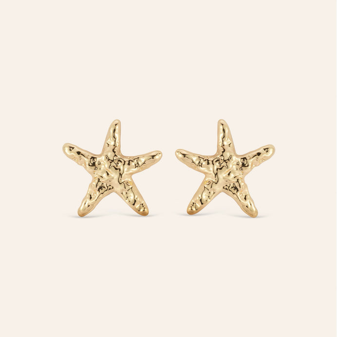 Hammered Gold Star Fish Stud Earrings on Cream Background