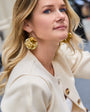 Woman wearing gold earrings and a cream-colored coat with blurred background