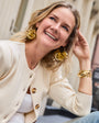 Woman wearing gold earrings and bracelet, smiling outdoors.