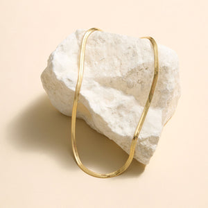 Gold Herringbone Necklace Staged on Stone with Cream Background