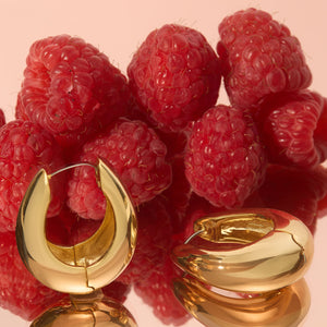 Gold Hoop Earrings Staged on Reflective Surface with Raspberries in Background