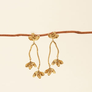 Gold Flower Drop Earrings Staged on Branch with Cream Background