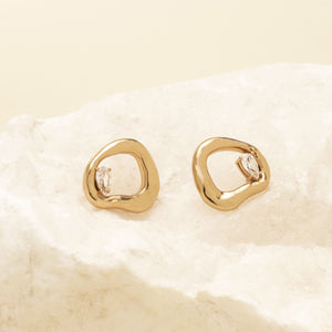 Gold Stud Earrings with Crystal Accent Staged on Stone with Cream Background