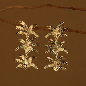 Gold Palm Dangle Earrings Staged Hanging off Branches with Brown Background