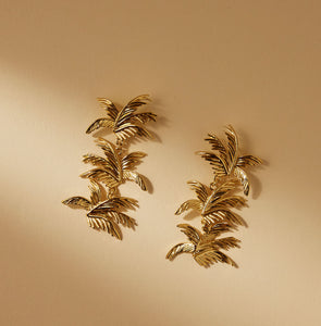 Gold Palm Dangle Earrings Staged on Cream Surface
