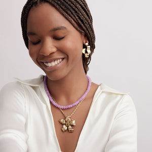 Large Wavy Gold Hoop Earrings Styled on Model in Purple Strand Necklace and Gold Flower Pendant Necklace