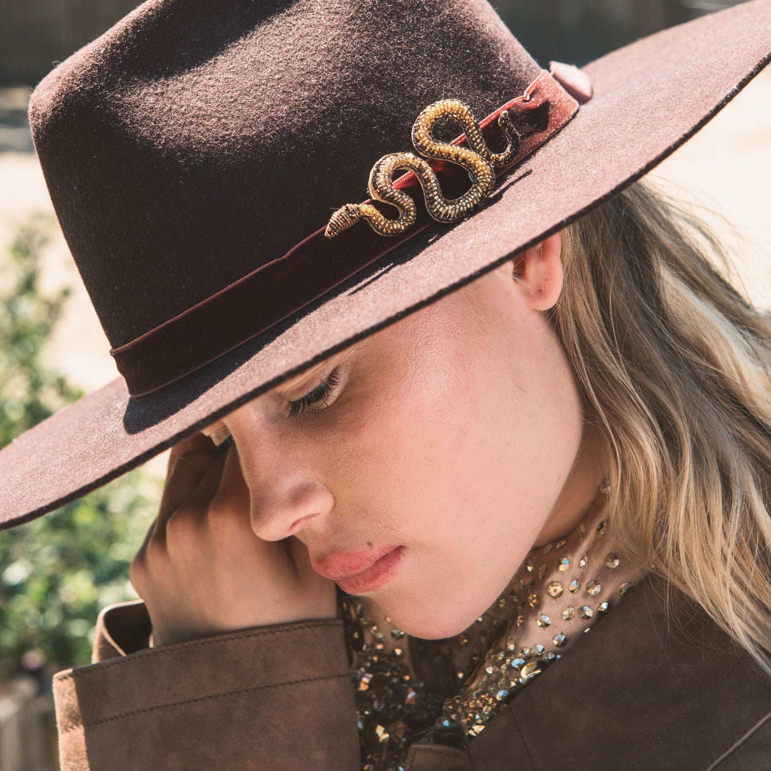 Woman wearing a brown hat with decorative brooch elements, looking downwards.