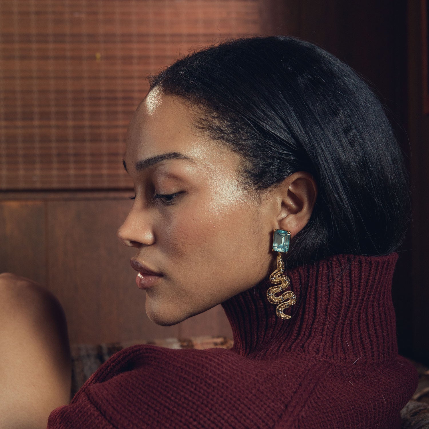 Woman wearing a maroon sweater and snake-shaped earrings with a blurred background