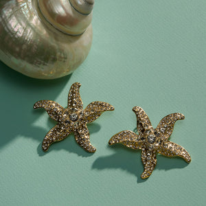Crystal and Gold Starfish Earrings Staged with a Shell on Green Surface
