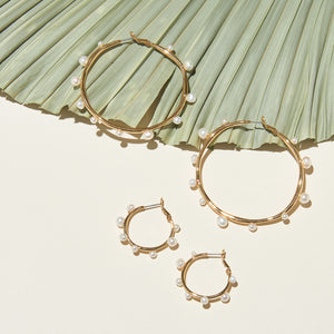 Gold and Multi-Sized White Pearl Hoop Earrings Styled with Larger Multi-Sized White Pearl and Gold Hoops on Palm Plant