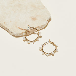 Gold and Multi-Sized White Pearl Hoop Earrings Staged on Cream Background with Stone Accent