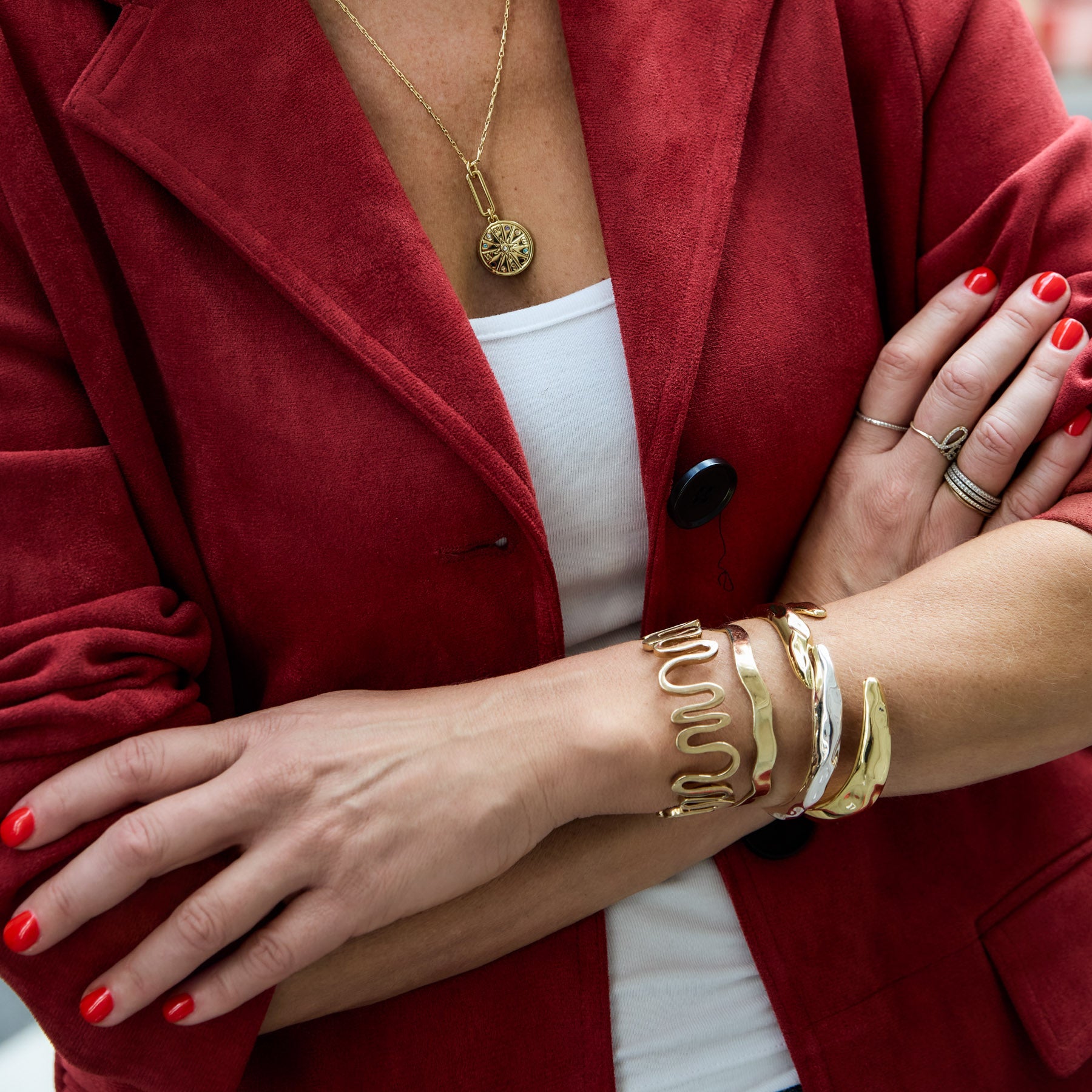 Person wearing gold bracelets and rings with a red coat and white top.