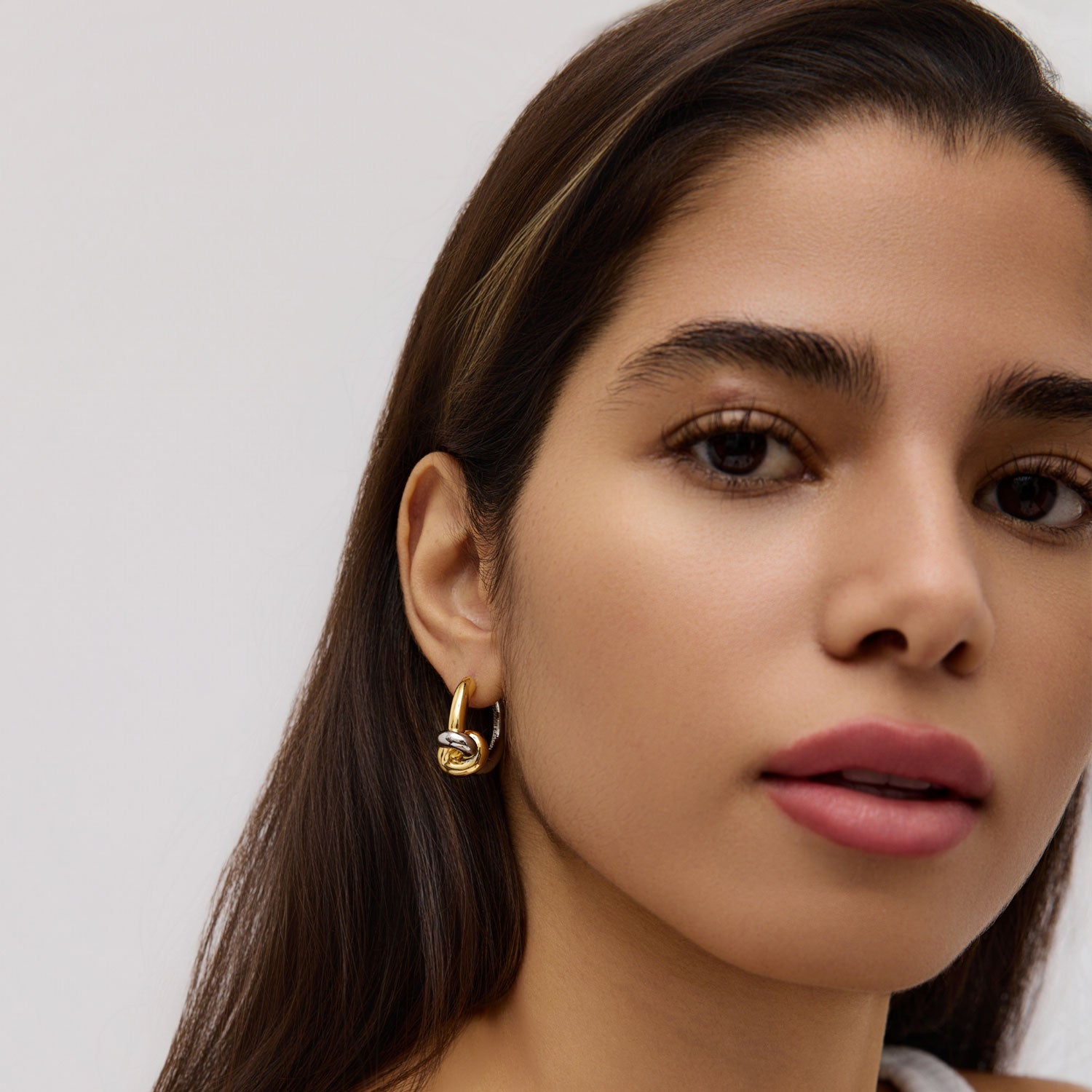 Close-up of a woman wearing a gold and silver earring against a neutral background