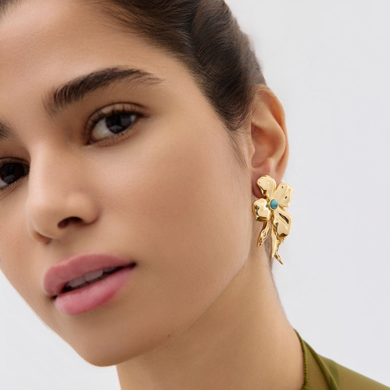 Close-up of a woman wearing a gold earring with a blue gemstone on a neutral background