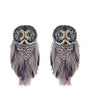 A pair of owl-shaped earrings made with gray and black feathers, silver rhinestones, and yellow eyes, shown against a plain white background.