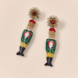 Green, Red, and Gold Beaded Nutcracker Drop Earrings on Tan Background