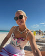 Woman sitting on a beach chair at a beach with sunglasses and a colorful swimsuit.