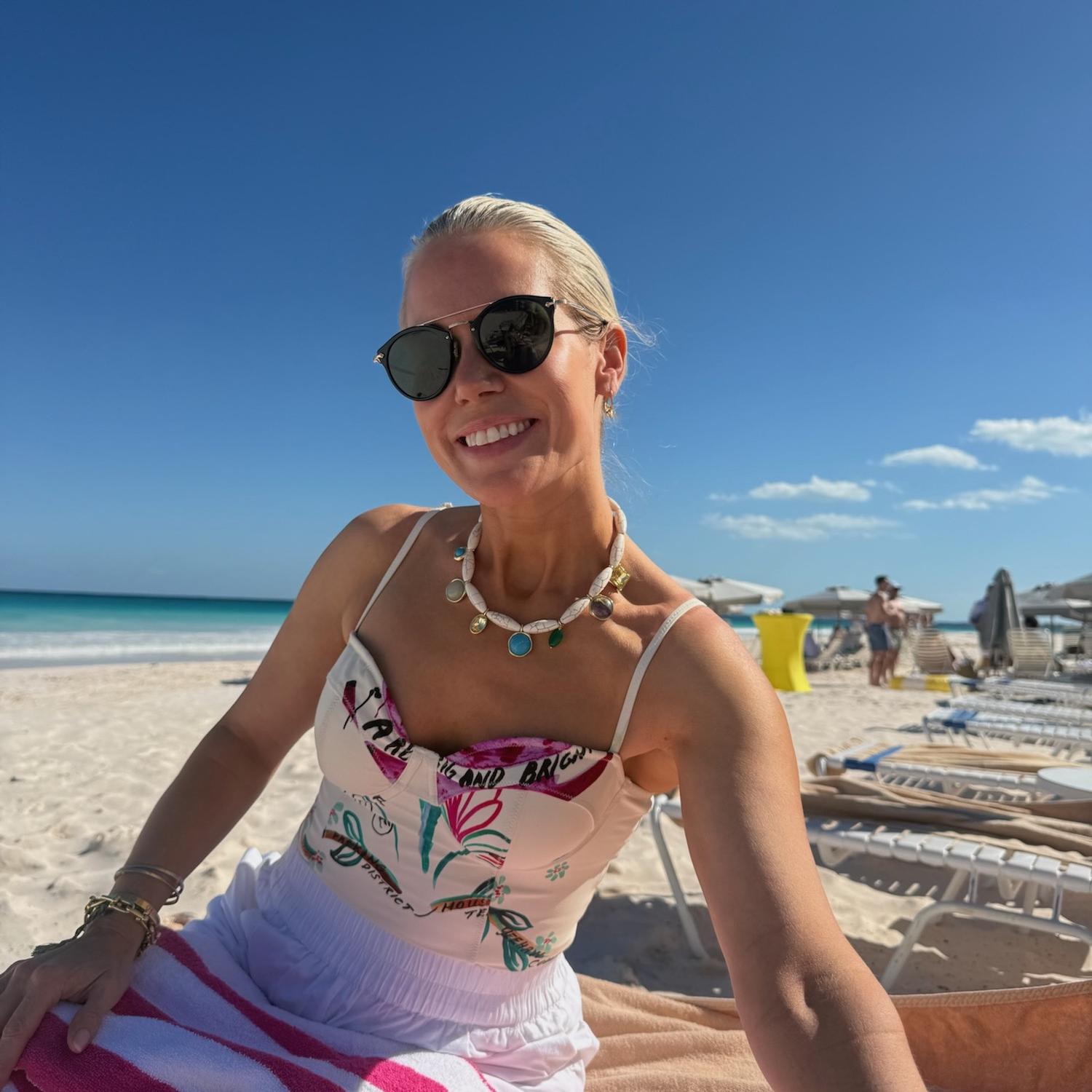 Woman sitting on a beach chair at a beach with sunglasses and a colorful swimsuit.