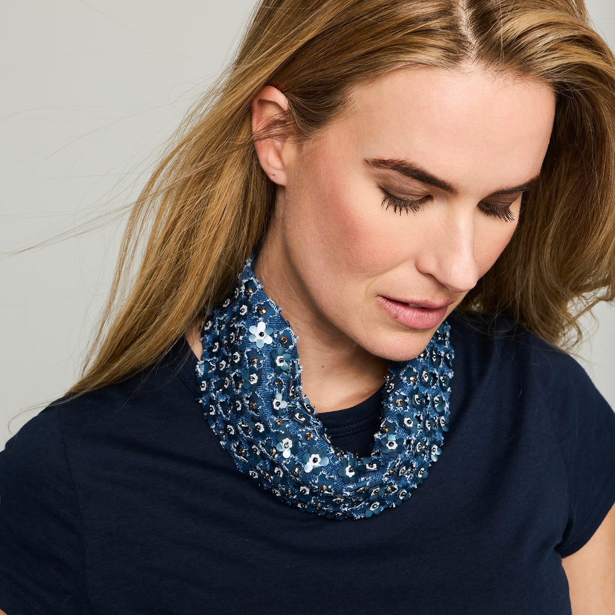 Blue scarf necklace featuring floral and beaded embellishments throughout on model looking down