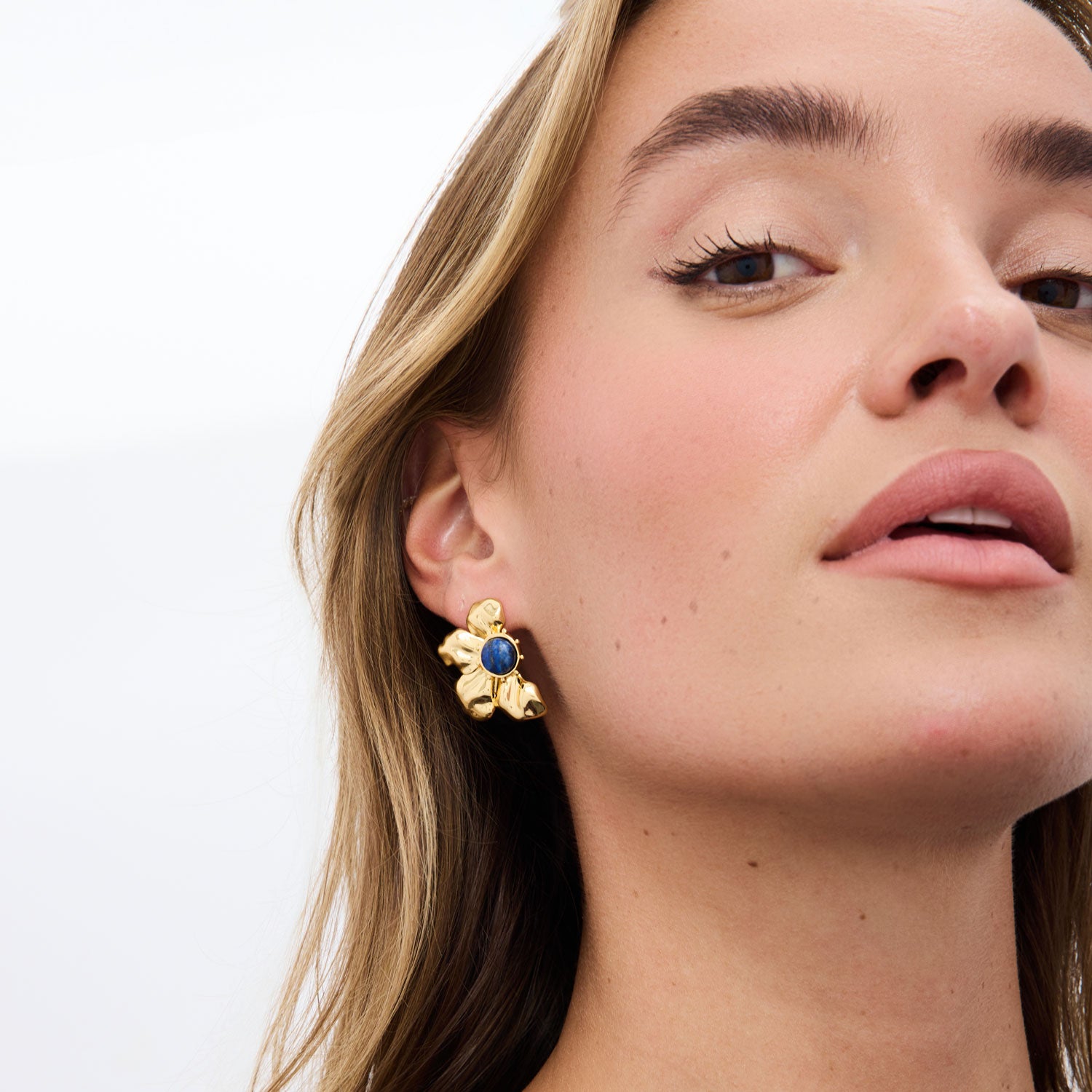 Close-up of a woman wearing gold earrings with a blue gemstone on a white background