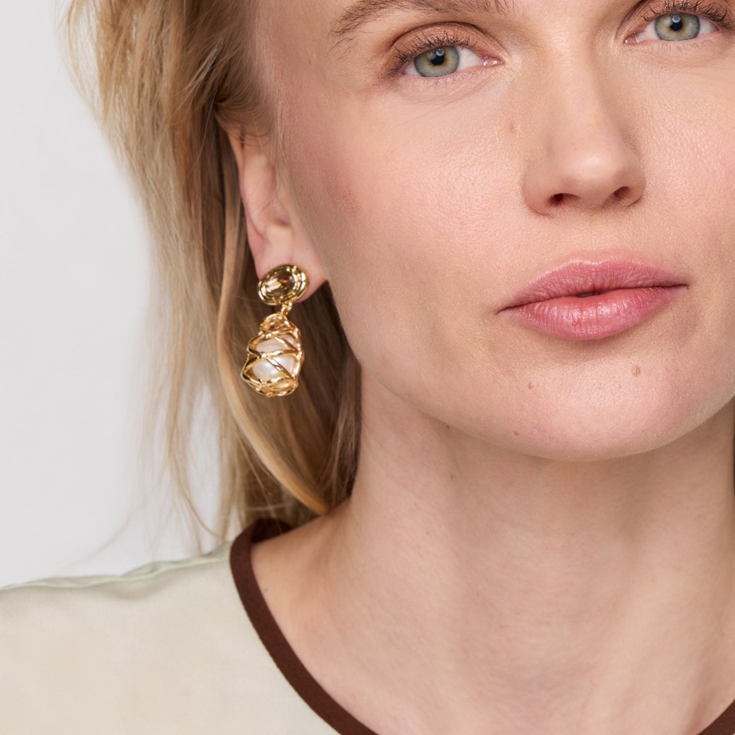 Close-up of a woman wearing gold earrings with a plain background