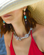 Model wearing a chunky beaded necklace with long fish and shell drop earrings while wearing a hat