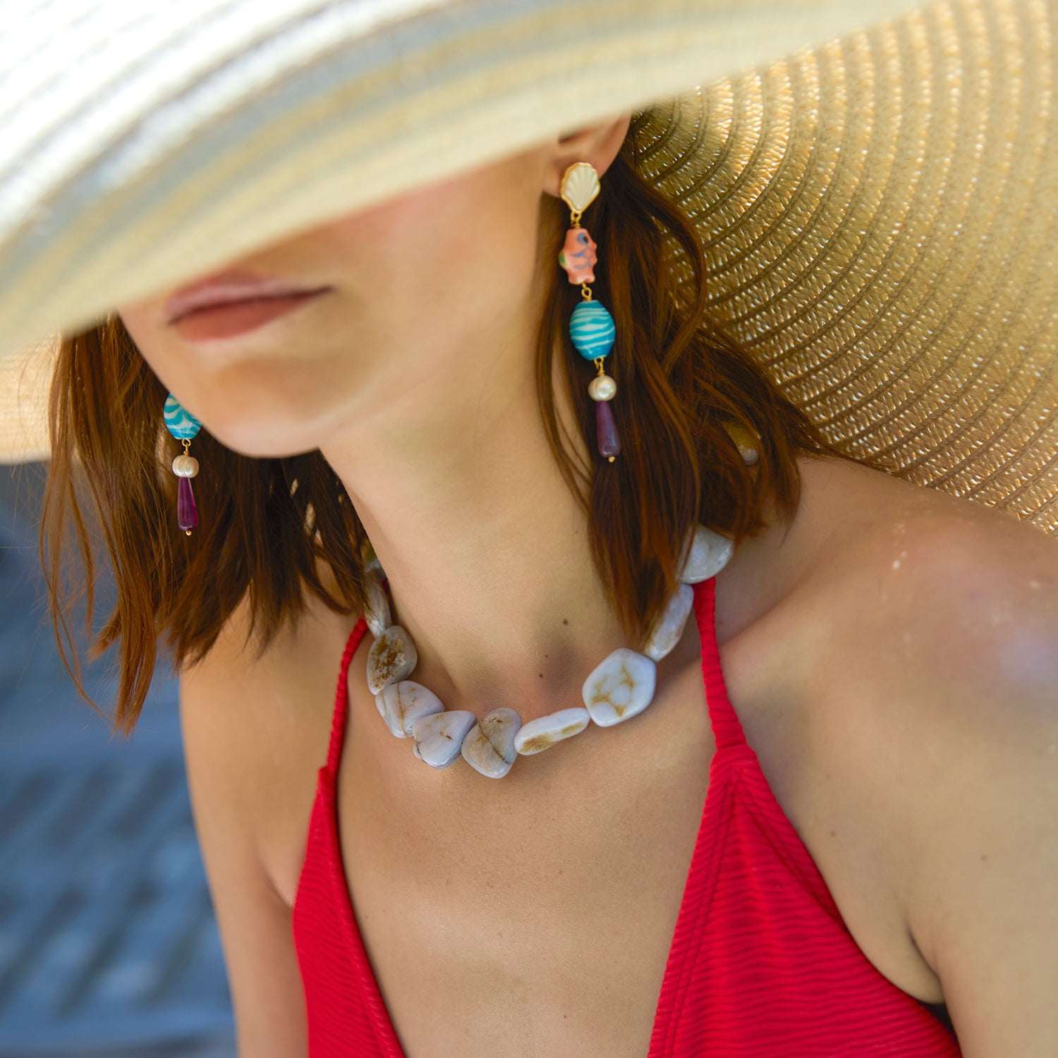Model wearing a chunky beaded necklace with long fish and shell drop earrings while wearing a hat