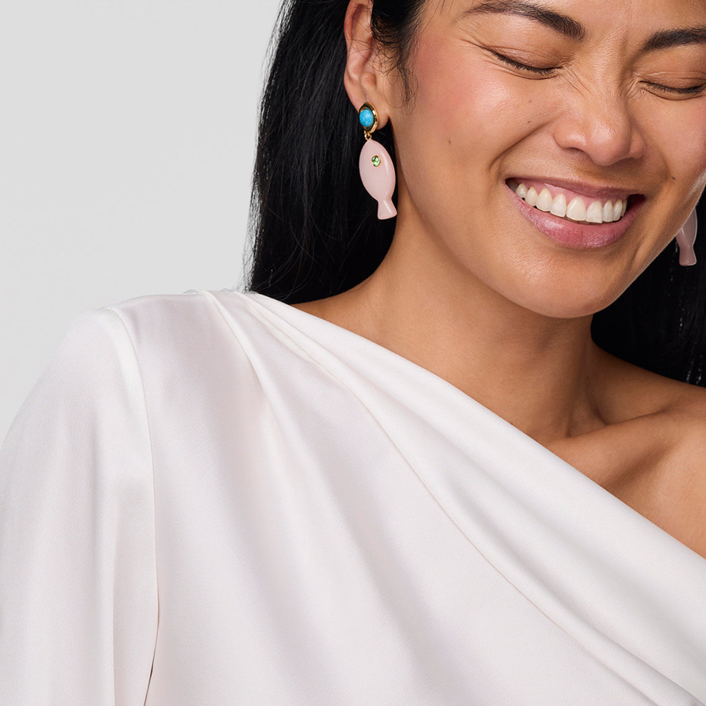 Woman wearing pink earrings with a white top against a light gray background