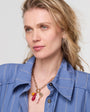 Woman wearing a blue shirt with a necklace featuring a red pendant against a plain background