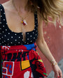Person wearing a black polka dot top and colorful skirt with a gold charm necklace and bracelet.