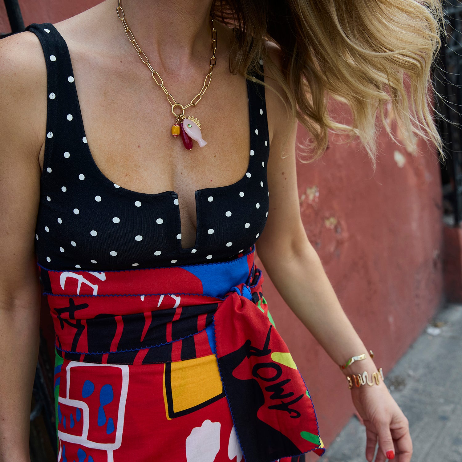 Person wearing a black polka dot top and colorful skirt with a gold charm necklace and bracelet.