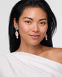 Woman wearing a white off-shoulder top with pink earrings on a light gray background